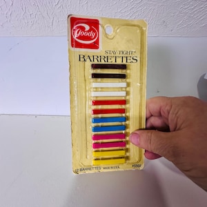 Puede incluir: Un paquete de 12 pasadores Goody Stay-Tight en un blíster de plástico vertical. El conjunto incluye dos unidades de cada color: marrón oscuro, blanco, rojo, azul, rosa y amarillo. El envase muestra el logotipo Goody y 12 BARRETTES.