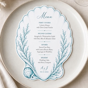 May include: A die-cut menu card shaped like a scallop shell, featuring teal ink illustrations of seaweed and a small shell at the base. The text lists a four-course meal including Lobster Bisque, Arugula & Watermelon Salad, Seared Sea Bass, and Wedding Cake, with the initials A & J and the date 06.15.2024.