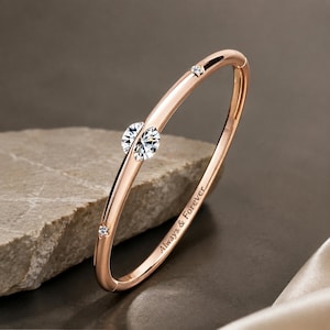 Op de afbeelding: Een roségouden armband met een centrale ronde heldere edelsteen, twee kleine stervormige accenten met ingelegde heldere steentjes en de gegraveerde tekst Always & Forever op het gladde, gepolijste metalen oppervlak.