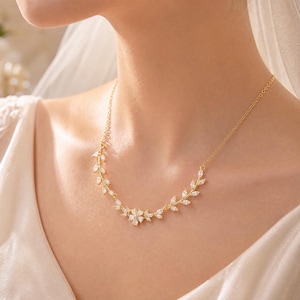 May include: A gold-toned necklace featuring a delicate vine-like design adorned with marquise-cut clear stones. The centrepiece consists of a small floral arrangement made of five pear-shaped stones, flanked by symmetrical leaf-shaped accents.