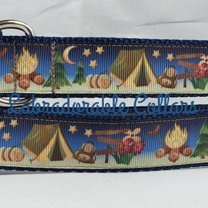 May include: Two blue dog collars with a camping themed print. The print features a campfire, tent, and stars on a white background. The collars are adjustable and have a metal buckle.