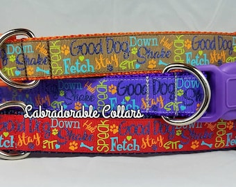 May include: Three dog collars with colorful patterned fabric featuring the words "Good Dog", "Fetch", "Stay", "Sit", "Down", "Heel", "Speak", and paw prints. The collars are layered on top of each other, with the top collar being brown, the middle collar being purple, and the bottom collar being red.