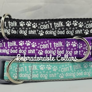 Puede incluir: Tres collares para perros con un patrón de huella de pata y el texto "Can't talk. Doing bad dog shit." en blanco. Los collares son negro, morado y azul verdoso.