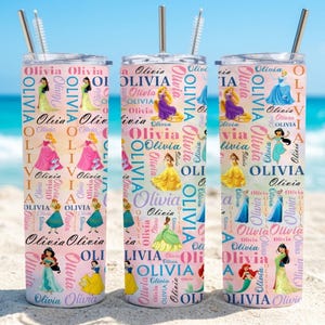 May include: Three personalized tumblers with princess illustrations and the name "Olivia" repeated in a pink and white pattern. Each tumbler has a silver straw and a lid. The background shows a beach and ocean.