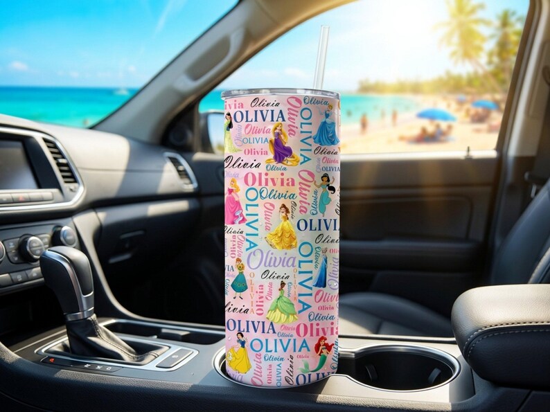 May include: A pink tumbler with a straw, featuring the name "Olivia" in a repeating pattern with princess illustrations. The tumbler is cylindrical and appears to be stainless steel. The background shows a car interior and a beach scene.
