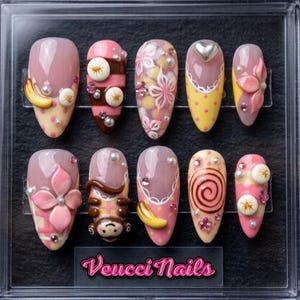 Könnte beinhalten: Ein Set aus zehn mandelförmigen Press-on-Nägeln in einer durchsichtigen Box mit der Aufschrift Veucci Nails. Die Nägel zeigen verschiedene 3D-Designs, darunter rosa Blumen, gelbe Bananen, ein brauner Affe, weiße Perlen und rosa Strasssteine.