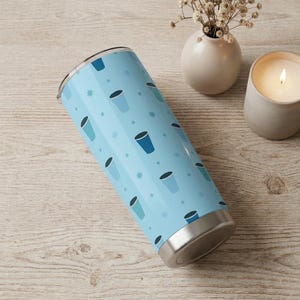 May include: A light blue insulated tumbler with a repeating pattern of blue coffee cup illustrations and small star shapes. The tumbler has a silver base and a black lid. The design is modern and suitable for hot or cold beverages.