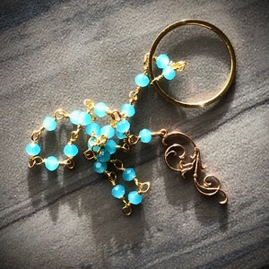 May include: A gold chain necklace with a blue gemstone pendant and a gold circle charm. The necklace is made of small, round blue beads and gold wire.