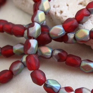 May include: A strand of red and iridescent glass beads. The beads are faceted and have a slightly irregular shape.