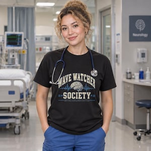 Könnte beinhalten: Ein schwarzes Kurzarm-T-Shirt mit einem Grafikdruck, der den Text "WAVE WATCHER SOCIETY" in Beige, eine zentrale Gehirnillustration und blaue EKG-Wellenlinien zeigt. Ein blaues Stethoskop liegt um den Hals über dem T-Shirt.