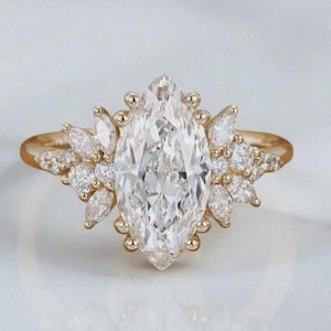 May include: A gold ring featuring a large marquise-cut center stone surrounded by a cluster of smaller marquise and round-cut white stones. The band is polished gold, and the setting creates a symmetrical, multi-stone arrangement on the finger.
