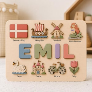 May include: A wooden name puzzle featuring the name EMIL in large, colorful letters. Surrounding the name are eight wooden cutouts with labels: Denmark Flag, Viking Ship, Windmill, Little Mermaid, Swan, Castle, Bicycle, and Tulip.