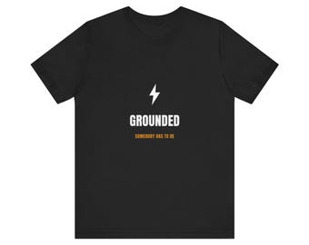 Puede incluir: Una camiseta negra de manga corta que presenta un icono de rayo blanco sobre la palabra GROUNDED en letras mayúsculas blancas, con la frase SOMEBODY HAS TO BE impresa en letras mayúsculas naranjas más pequeñas justo debajo del texto principal.