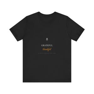 Może przedstawiać: Czarny t-shirt z krótkim rękawem z małą białą ikoną botaniczną nad napisem GRATEFUL w kolorze białym, thankful złotą czcionką kursywą oraz napisem & TRIPLE CHECKING THE LABEL małymi białymi wielkimi literami na środku klatki piersiowej.
