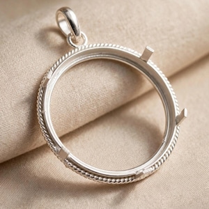 Op de afbeelding: Een ronde zilveren hangerzetting met een gedraaide touwstructuur langs de buitenrand. Het frame bevat vier gelijkmatig verdeelde klauwen die naar binnen wijzen om een edelsteen vast te zetten, bekroond met een glad, gepolijst zilveren oogje.