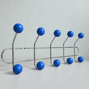 May include: A wall-mounted coat rack featuring a horizontal silver-toned metal frame with five upper and four lower hooks. Each hook is tipped with a smooth, round, bright blue ball. The structure is designed for hanging garments and accessories.