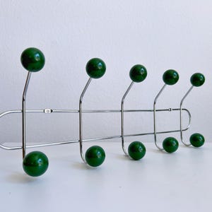 May include: A mid-century modern coat rack with a chrome finish and six dark green ball-shaped hooks. The hooks are evenly spaced along a horizontal bar, with three hooks on top and three below.
