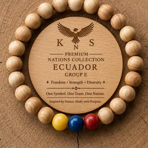 Könnte beinhalten: Eine kreisförmige Holzplakette mit einer Adlergrafik und dem Text "PREMIUM NATIONS COLLECTION ECUADOR GROUP E", umgeben von einem Perlenarmband. Das Armband besteht aus hellbraunen Holzperlen mit drei markanten gelben, blauen und roten Perlen.