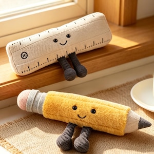 May include: Two plush school supply toys: a ruler and a pencil. The ruler is beige with black markings and a smiling face. The pencil is yellow with a pink eraser and a gray tip, also with a smiling face. Both have gray legs.
