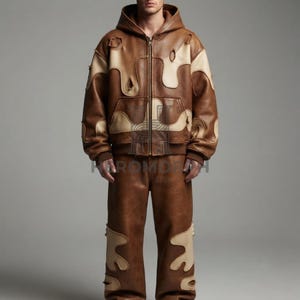 Könnte beinhalten: Ein Set aus einer braun-beigen Lederjacke mit Kapuze und einer passenden Hose. Die Jacke hat einen durchgehenden Frontreißverschluss, lange Ärmel und abgenutzte Details. Beide Teile sind mit großen, organisch geformten, cremefarbenen Lederapplikationen versehen.