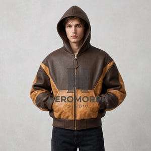 Può includere: Una giacca con cappuccio caratterizzata da un design a blocchi di colore marrone scuro e marrone chiaro. Il capo presenta una chiusura frontale con zip, maniche lunghe con polsini a coste e una finitura testurizzata. Il testo HEROMORPH STUDIO è stampato al centro.