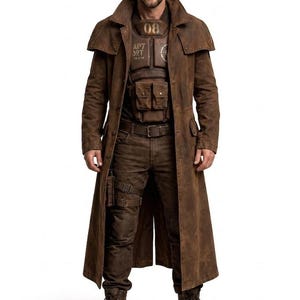 Könnte beinhalten: Ein langer, brauner Duster-Mantel in Used-Optik über einer dunkelbraunen taktischen Weste mit der Aufschrift 08 und AP7 ORT, dazu eine passende braune Hose mit Beinholster und braune Schnürstiefel. Das Outfit hat ein robustes, abgenutztes Design.