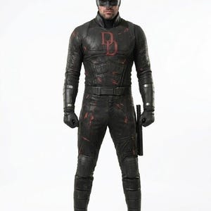 Puede incluir: Una figura de acción de un personaje con un traje táctico negro que presenta un emblema DD de color rojo oscuro en el pecho, una máscara negra a juego con pequeños cuernos, además de guantes y botas negras. El traje tiene texturas visibles.