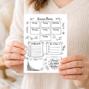 Op de afbeelding: Een zwart-wit business planner met secties voor elke dag van de week, wekelijkse doelen, top taken en ideeën. De planner is versierd met bloemen- en sterillustraties, en de tekst "Focus On What Matter" is ook opgenomen.