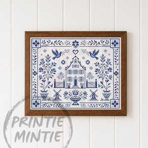 May include: A framed cross-stitch embroidery featuring a blue and white design of a central house, two birds, windmills, and floral motifs in urns. The artwork is enclosed in a dark brown wooden frame and displays a symmetrical pattern.
