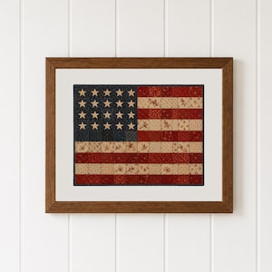 May include: A framed wall art piece featuring a patchwork quilt design of the American flag. The flag is composed of small square fabric patches in shades of deep red, cream, and navy blue, with cream-colored stars on a navy blue field.
