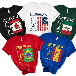 May include: Five short-sleeved t-shirts in black, white, red, green, and blue. Each shirt features a country's flag design with the country's abbreviation and the number 23. The shirts are for Canada, USA, Mexico, Brazil, and Spain.