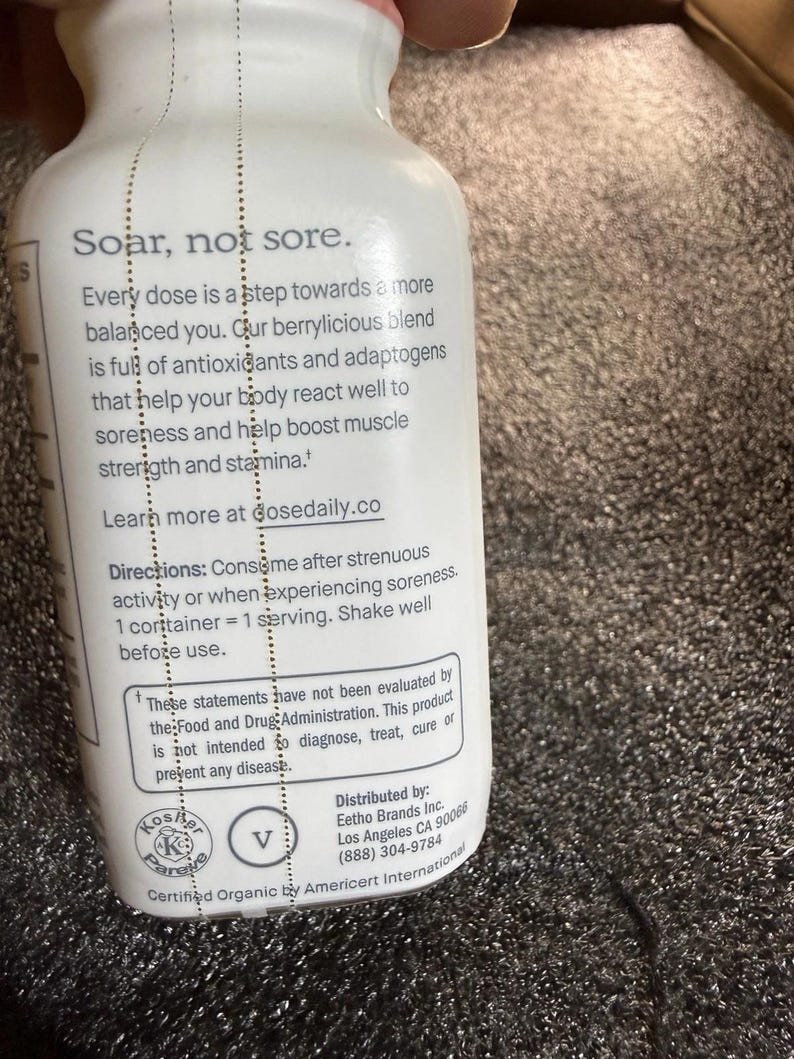 May include: A white plastic bottle with black text that reads: Soar, not sore. Every dose is a step towards a more balanced you. Our berrylicious blend is full of antioxidants and adaptogens that help your body react well to soreness and help boost muscle strength and stamina. Learn more at dosedaily.co. Directions: Consume after strenuous activity or when experiencing soreness. 1 container = 1 serving. Shake well before use.