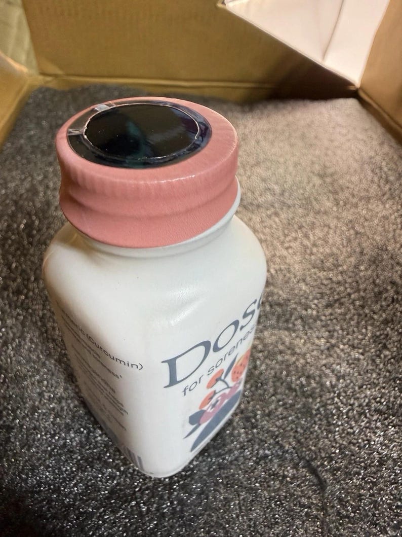 May include: A white plastic bottle with a light pink screw-on cap and a black circular seal on top. The label features the text "Dose" and "for soreness" along with a graphic illustration of orange and grey floral elements and text mentioning Curcumin.
