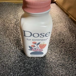 May include: A white plastic bottle with a pink cap containing a dietary supplement. The label features the text Dose for soreness and a graphic illustration of a strawberry and blueberries. The bottle has a net weight of 2.5 fl oz.