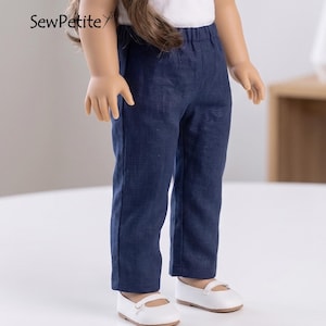 以下が含まれることがあります： 白いトップスとネイビーブルーのパンツを着用した人形。パンツはストレートレッグで、ウエストはゴム入りです。人形は白い靴も履いています。「SewPetite」の文字が左上に表示されています。
