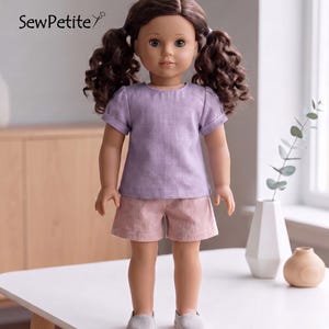 May include: A doll wearing a lavender short-sleeved top and pink shorts. The doll has brown curly hair in pigtails and is wearing gray shoes. The text "SewPetite" is in the upper left corner.