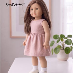 Peut inclure: Une poupée aux longs cheveux bruns et aux yeux verts vêtue d'une robe rose sans manches, de chaussettes blanches et de chaussures blanches. La robe a une taille froncée. Le texte "SewPetite" est dans le coin supérieur gauche.