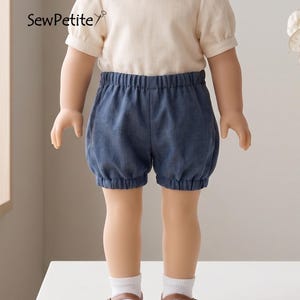 May include: A doll dressed in a cream blouse with a Peter Pan collar and short, puffed sleeves. The doll is wearing blue bloomers and brown Mary Jane shoes. The text "SewPetite" is visible in the upper left corner.