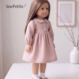 Pode incluir: Uma boneca vestindo um vestido rosa claro com gola Peter Pan e mangas compridas. O vestido tem uma frente abotoada e uma saia franzida. A boneca tem cabelo castanho comprido, olhos azuis e usa meias brancas e sapatos cinzentos. A imagem inclui o texto "SewPetite".