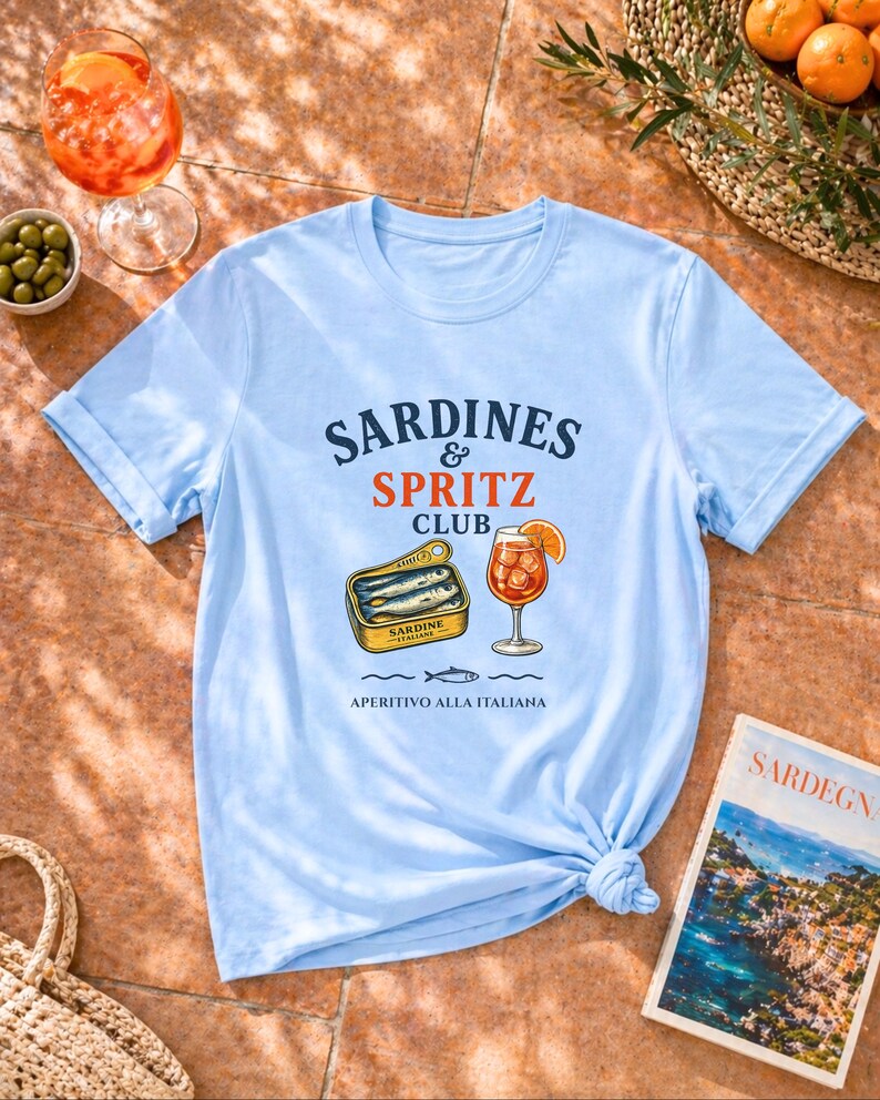 light blue sardines and spritz shirt flatlay, coastal summer tee, sardine graphic shirt, Mediterranean vacation outfit, amalfi shirt, sardegna