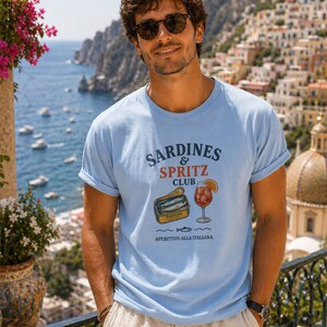 Italian summer shirt mockup on a man in Positano, blue graphic tee with sardines and spritz design, Amalfi Coast vacation outfit, Mediterranean summer fashion