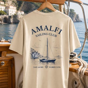 Natural Amalfi Sailing Club shirt hanging on a yacht with large nautical back print, inspired by sailing adventures and Italian coastal escapes.
