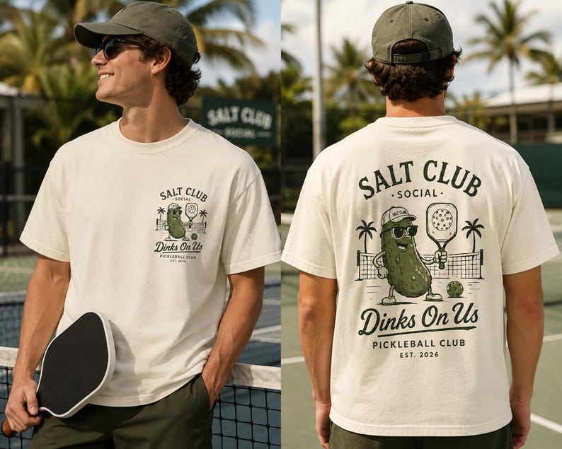 May include: An off-white short-sleeve t-shirt featuring a graphic of a pickleball-playing pickle wearing sunglasses and a cap. The front chest displays a small logo, while the back features a larger version with the text Salt Club Social Dinks On Us Pickleball Club Est. 2026.
