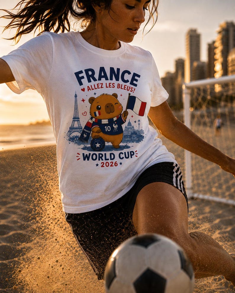 May include: White t-shirt with a graphic of a cartoon bear in a French football kit, holding a flag. The shirt displays the words "FRANCE" and "WORLD CUP 2026". The bear is wearing a jersey with the number 10.