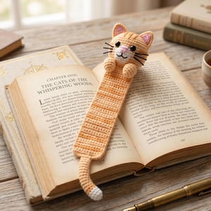 May include: Crocheted orange tabby cat bookmark with black whiskers, pink ears, and a white-tipped tail. The bookmark is placed in an open book with the title "The Cats of the Whispering Woods."
