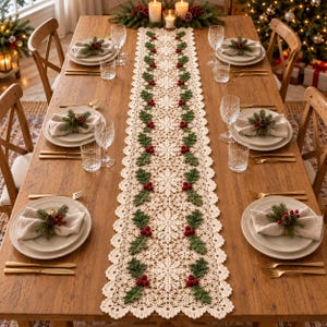 Puede incluir: Un camino de mesa largo de ganchillo color crema con un patrón repetitivo de hojas de acebo verdes y bayas rojas, sobre una mesa de madera con platos blancos, cristalería, cubiertos dorados y servilletas decoradas con acebo.