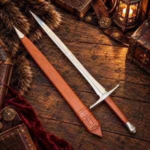 May include: A double-edged steel sword with a silver crossguard and a brown leather-wrapped handle, accompanied by a matching brown leather scabbard featuring a silver metal tip and a reinforced throat section with three horizontal bands.