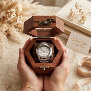 May include: A silver-toned analog wristwatch with a metallic link band and a round face featuring multiple sub-dials, housed inside an open, dark brown, hexagonal wooden box with a brass-colored metal latch closure and a soft brown interior cushion.