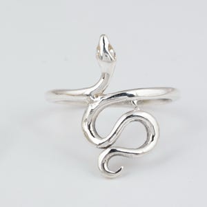 May include: A polished silver ring featuring a coiled snake design. The snake's head is positioned at the top, while its body curves downward to form the band of the ring. The metal has a smooth, reflective finish throughout the entire piece.