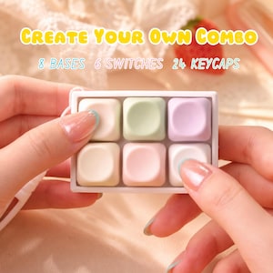 Può includere: Una piccola custodia rettangolare bianca contenente sei tasti quadrati color pastello. I tasti sono in tonalità di rosa, verde e bianco. Il testo in alto recita "CREATE YOUR OWN COMBO" con i dettagli "8 BASES 6 SWITCHES 24 KEYCAPS".
